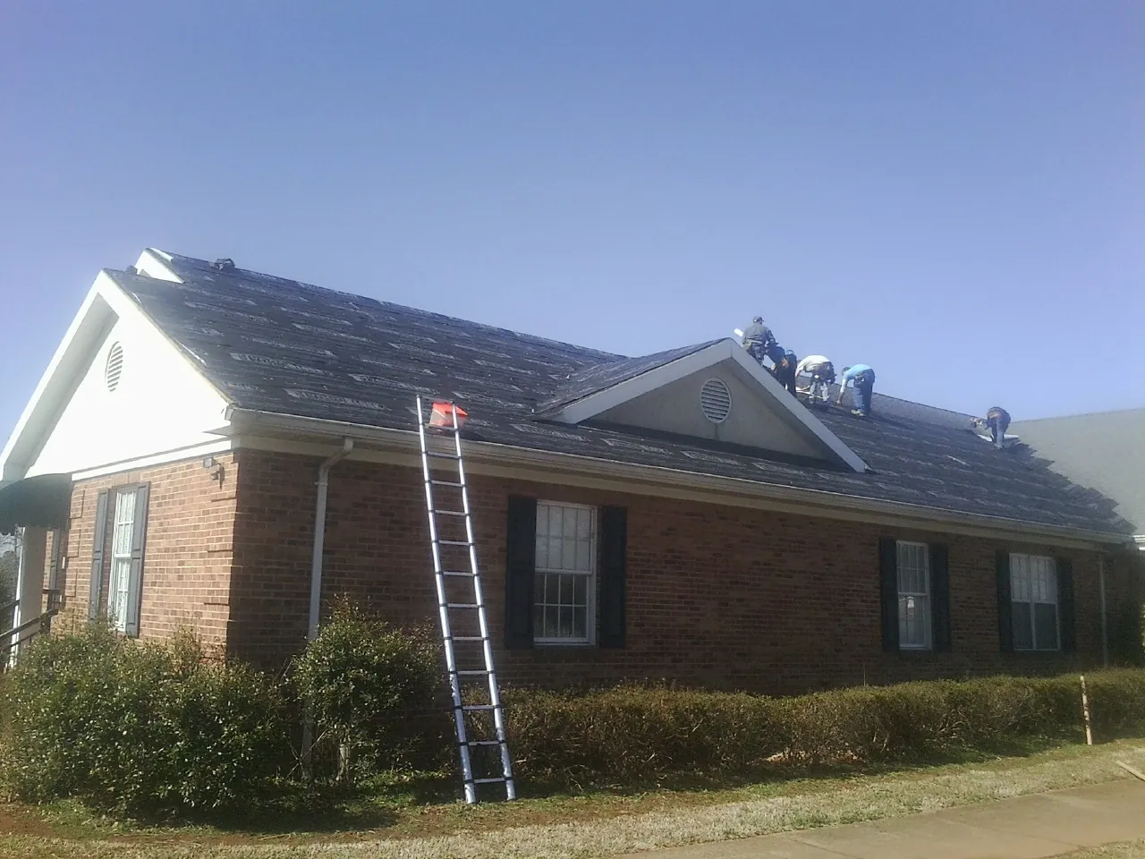 Crew tearing shingles off a brick ranch roof with a ladder set — Emergency Roof Repair work by our crew in Dyer