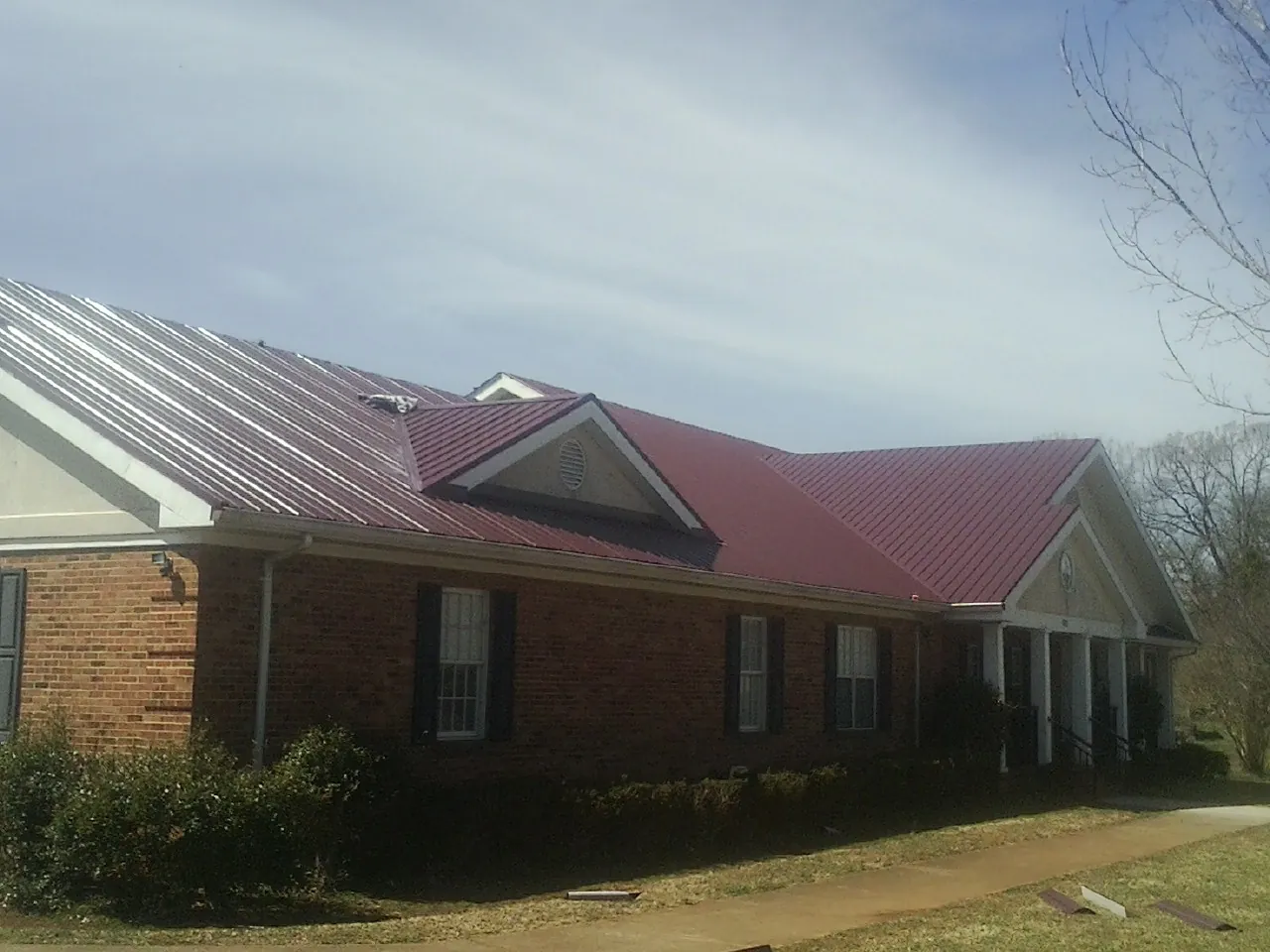 Red metal roof with gabled entries on a long brick building, from a Hail Damage Roof Repair job in Dyer