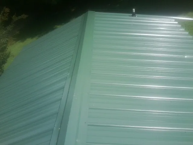 New green metal panels meeting at the ridge of a roof — Flat Roof Repair work by our crew in Dyer