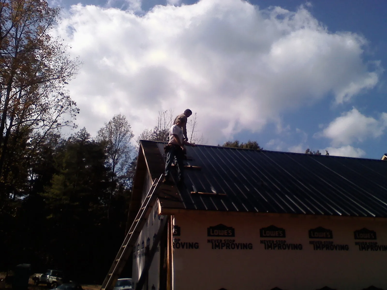 Roofer fastening dark metal panels high against a cloudy sky, from a Roof Inspection job in Dyer